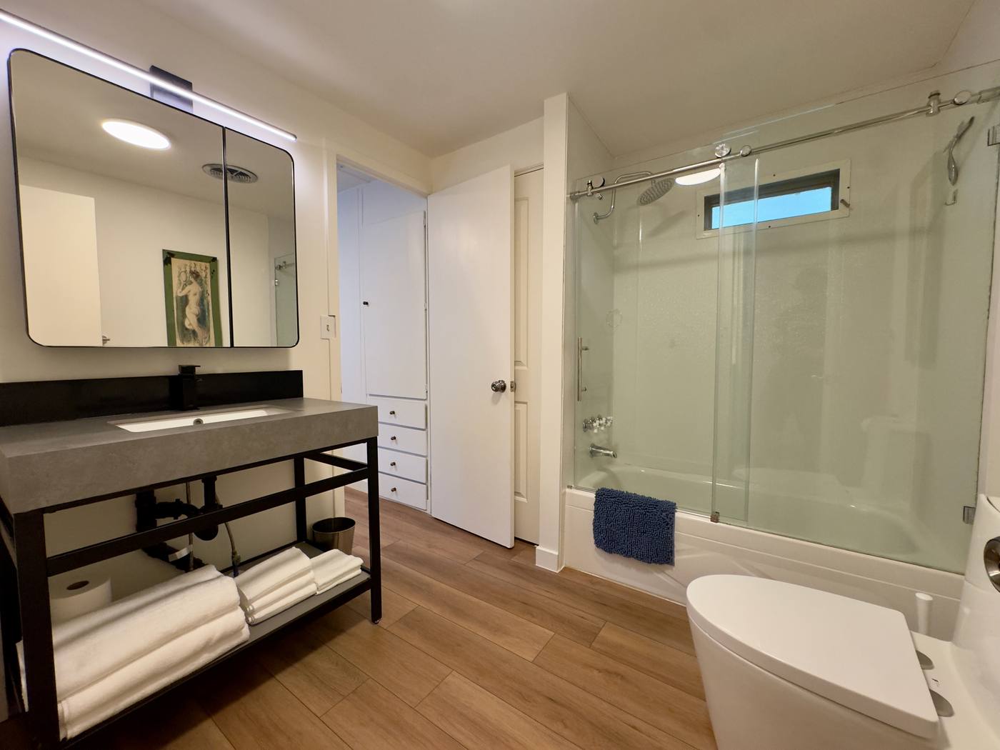 First bathroom with a concrete-topped vanity on a black steel frame and a glass-door tub and shower